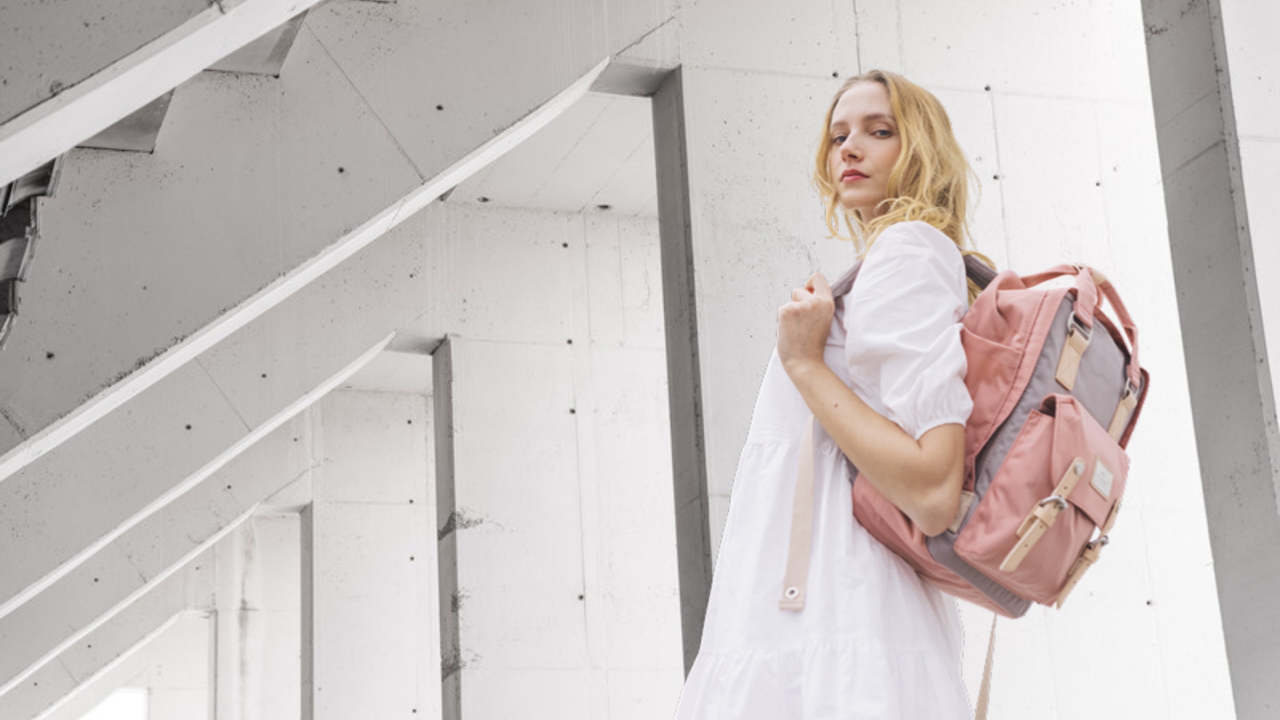 Frau mit rosafarbenem Doughnut Macaroon Rucksack vor Betonarchitektur