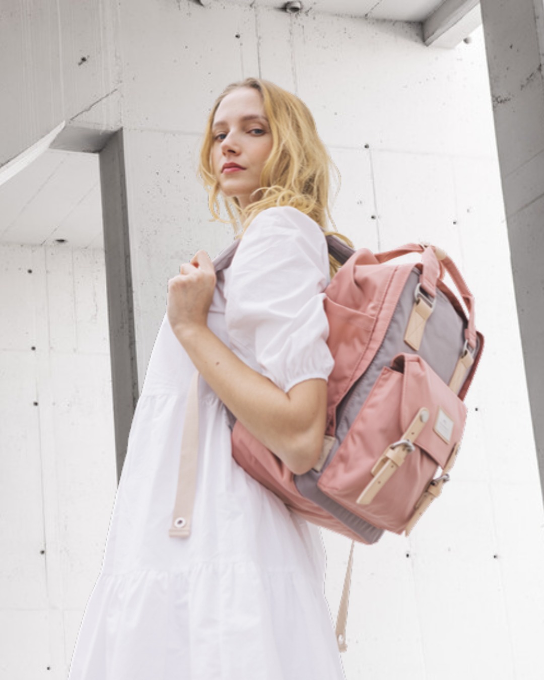 Frau mit rosafarbenem Doughnut Macaroon Rucksack vor Betonarchitektur